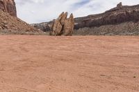 an odd rock on a desert area with mountains in the background, with white clouds