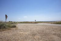 a dirt road with no traffic in a dry field area and signs on poles that point towards the open desert area