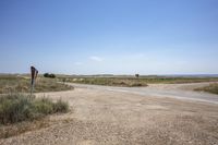 a dirt road with no traffic in a dry field area and signs on poles that point towards the open desert area