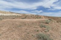 an empty dirt path in the middle of desert land with clouds above the horizon and dirt on the ground