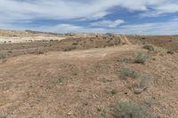 an empty dirt path in the middle of desert land with clouds above the horizon and dirt on the ground