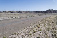 a desert with sand and rocks in the background and vegetation near the road on either side