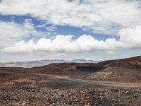 a dirt road that has been paved in two directions, through the desert with mountains in the background