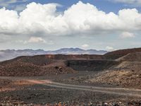 a dirt road that has been paved in two directions, through the desert with mountains in the background