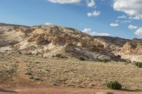 a dirt covered mountain sitting in the middle of the desert with vegetation on both sides