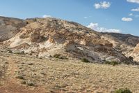 a dirt covered mountain sitting in the middle of the desert with vegetation on both sides