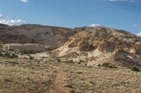 a dirt covered mountain sitting in the middle of the desert with vegetation on both sides