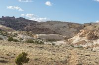 a dirt covered mountain sitting in the middle of the desert with vegetation on both sides