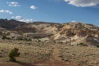 a dirt covered mountain sitting in the middle of the desert with vegetation on both sides