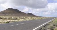 two lanes of asphalt with mountains in the distance, and a grassy field below them