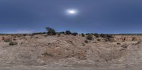 a wide angle picture shows the sun on top of a mountain in the desert beneath a blue sky