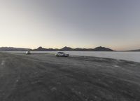 two vehicles parked at an empty frozen lake in the desert during a sunset scene with a blue sky