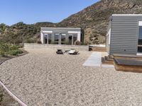 a car is parked by a house and mountain view of the desert behind it with a couple of beds in between