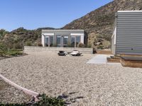 a car is parked by a house and mountain view of the desert behind it with a couple of beds in between