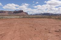 a dirt road through the desert with mountains in the distance while blue sky and clouds are visible overhead