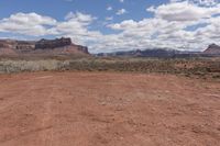 a dirt road through the desert with mountains in the distance while blue sky and clouds are visible overhead