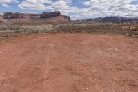 a dirt road through the desert with mountains in the distance while blue sky and clouds are visible overhead