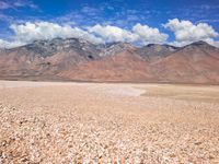 a man walking with his backpack in the middle of the desert with mountains behind him