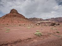 a big red rock sitting in the middle of desert desert area with clouds overhead on a cloudy day