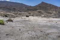 the barren terrain is full of dirt and some plants on top of it while the mountains are in the background