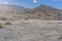 the barren terrain is full of dirt and some plants on top of it while the mountains are in the background