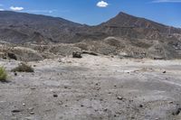 the barren terrain is full of dirt and some plants on top of it while the mountains are in the background