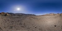 a wide angle view of the barren landscape of desert mountains and hills with a bright sun in a blue sky