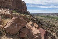 a big rock sitting next to a lush green hillside on top of a hill of red rocks