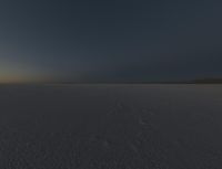 a lone person stands on the snow near the horizon, in the dark sky over some land