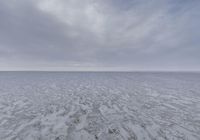 a lone snowboarder walks across the ice on a large flat plain at the bottom of the ocean