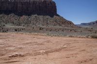 a dirt road through a desert plain with a mountain behind it and a clear blue sky in the background