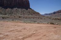 a dirt road through a desert plain with a mountain behind it and a clear blue sky in the background