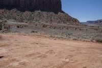 a dirt road through a desert plain with a mountain behind it and a clear blue sky in the background