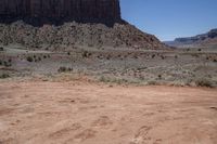 a dirt road through a desert plain with a mountain behind it and a clear blue sky in the background