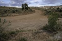 the dirt road is empty and the storm is coming in and the grass is very brown