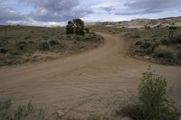 the dirt road is empty and the storm is coming in and the grass is very brown