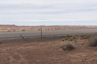 a sign is posted near an empty country road in the desert plain, in front of a desert plain