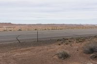 a sign is posted near an empty country road in the desert plain, in front of a desert plain