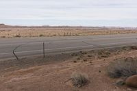 a sign is posted near an empty country road in the desert plain, in front of a desert plain