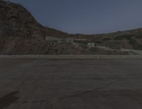 a lone motorcycle in the middle of the desert at dusk, with a building in the back ground