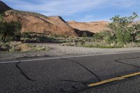 empty highway going up hill towards a cliff wall in desert landscape area with red rocks