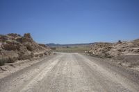 an empty road in the desert near rocky terrains under a blue sky with only one person