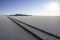 two tire tracks are pictured in an empty, vast place with a blue sky background