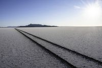 two tire tracks are pictured in an empty, vast place with a blue sky background