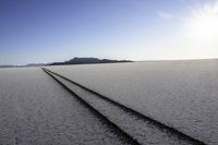 two tire tracks are pictured in an empty, vast place with a blue sky background