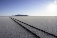 two tire tracks are pictured in an empty, vast place with a blue sky background