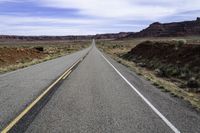 a road stretching into the distance in the desert with a mountain and cliff in the background