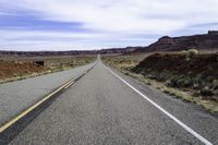 a road stretching into the distance in the desert with a mountain and cliff in the background