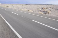 a desert road that has two lanes, painted white in the distance are yellow dry bushes
