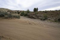 a desert road through the hills with some rocks and bushes on either side of the path